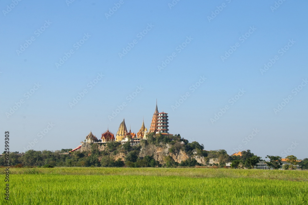 Obraz premium Wat Tham suea or Tiger cave temple on hill surrouned rice paddy and light blue sky in Kanchanaburi province, Thailand.