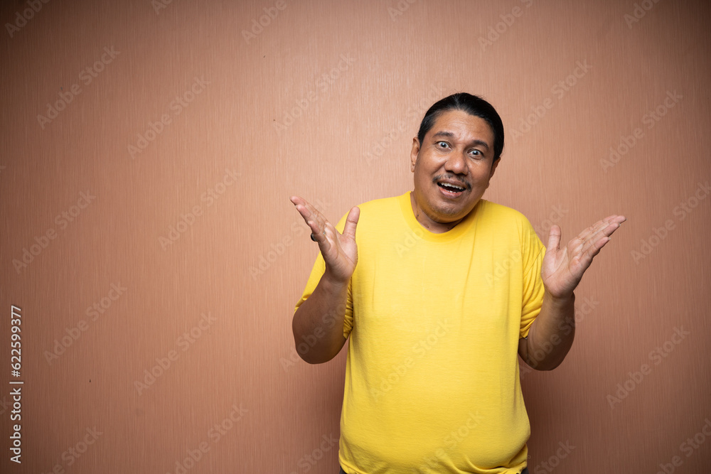 old asian man wearing yellow tshirt with open arm or welcoming gesture in plain background old asian man wearing yellow tshirt with open arm or welcoming gesture in plain background