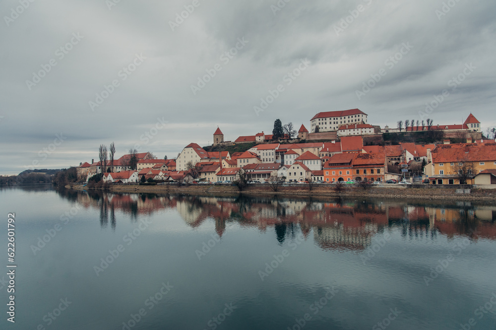 A panoramic view of Ptuj, Slovenia, reveals its charming old town, majestic castle, and a meandering river under a cloudy sky. A panoramic view of Ptuj, Slovenia, reveals its charming old town, majestic castle, and a meandering river under a cloudy sky.