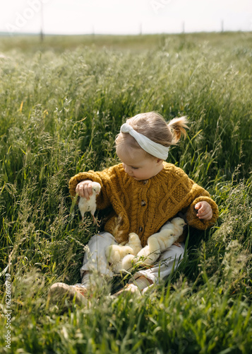 little girl playing with chicks in a field sitting on green grass