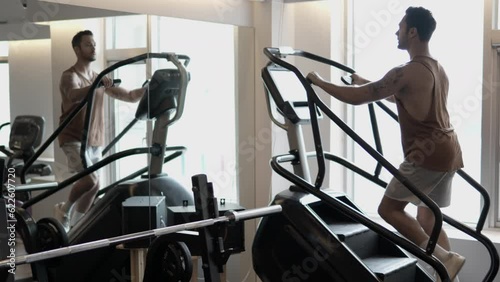 Sporty Man Doing Cardio on Stair Stepper Machine At Gym, One Male Reflected in Mirror Using Stepmill Stair Climbing Equipment - slow motion