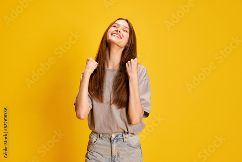 Portrait of young beautiful, emotive girl expressing happiness, success and win against yellow studio background. Concept of human emotions, fashion, youth, lifestyle, female beauty, ad