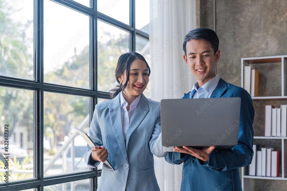 Young business man holding a laptop while discussing new project with his female collegue in office Young business man holding a laptop while discussing new project with his female collegue in office