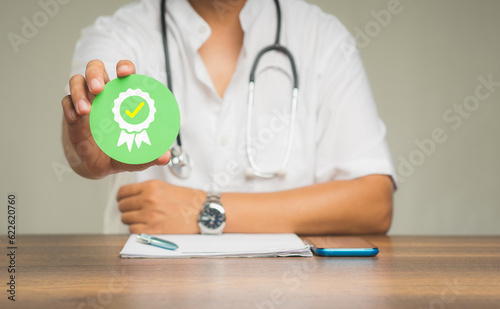 Doctor holding a quality assurance symbol while sitting at the table in the hospital.