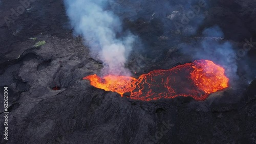 Crater in an erupting volcano in Iceland filled with molten lava that is flowing out of it
