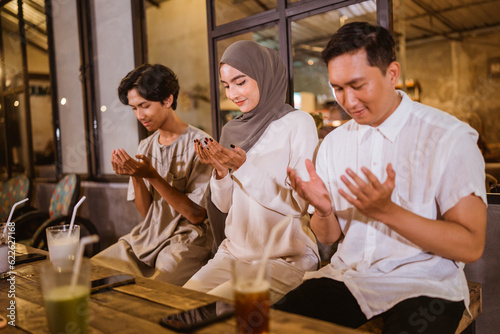 Asian Muslims celebrating Eid Mubarak pray before eating during an outdoor communal meal