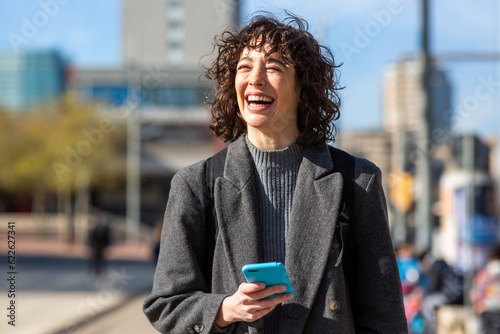 Beautiful woman in coat with mobile phone walking outside in the city © mimagephotos