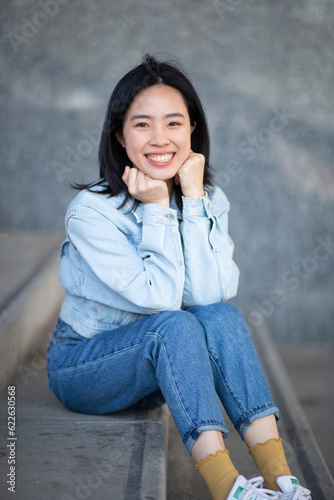 smiling young asian woman sitting on steps with chin on hand