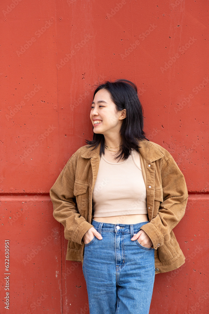 young asian woman smiling by wall