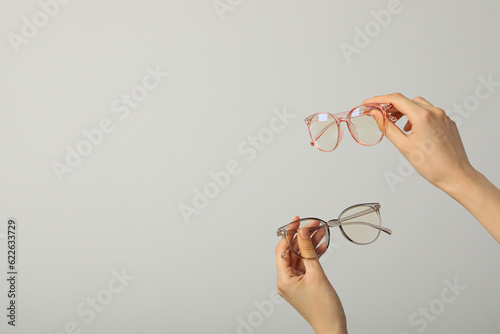 Glasses in female hands on light gray background  space for text