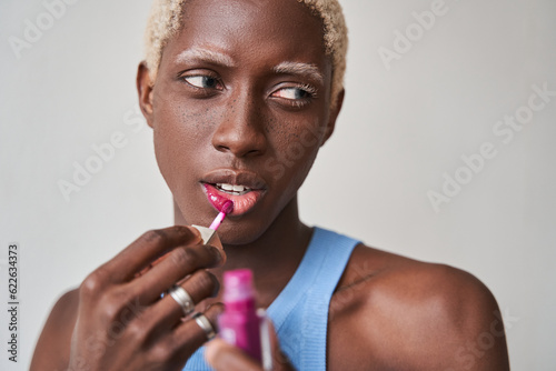 Photo of blonde haired feminine man applies lipstick wears makeup