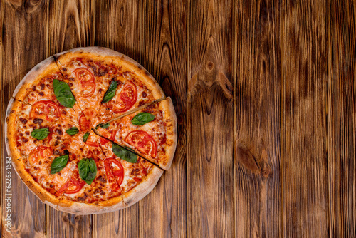 Delicious fragrant pizza-Margherita with mozzarella, tomatoes and basil on tomato sauce on woden background. Copy space photo