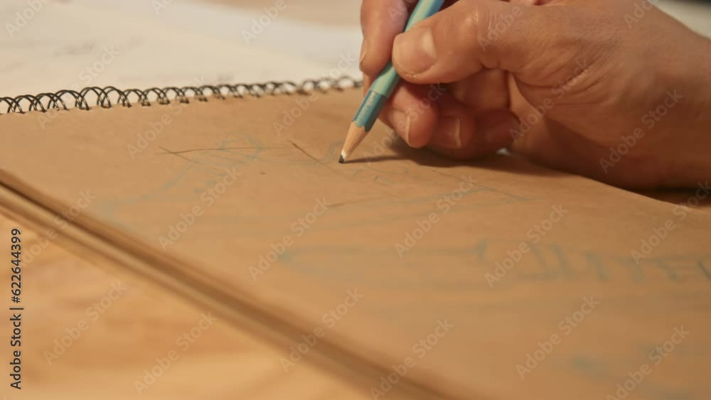 Close up of unrecognizable man holding pencil and drawing sketches of sneakers on craft paper indoors Close up of unrecognizable man holding pencil and drawing sketches of sneakers on craft paper indoors
