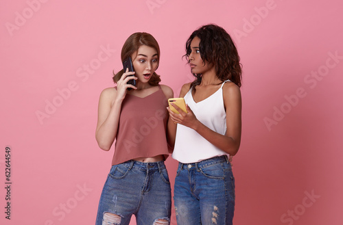 surprised young friends women show news on smartphone isolated on pink background.