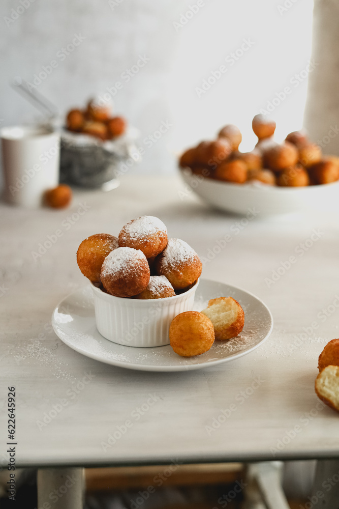 Rosy balls of delicious doughnuts in powdered sugar in a white ceramic bowl on the table. Still life with homemade food. Traditional oriental sweets and treats for the Hanukkah holiday. 