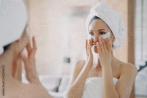 Girl applies eye patches, looks in mirror Fototapeta