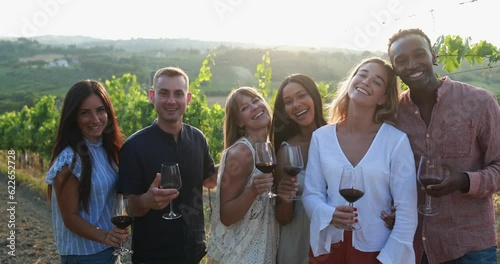 Happy adult friends having fun together drinking red wine and smiling on camera inside vineyards - Multiracial people doing party at summer time in countryside resort