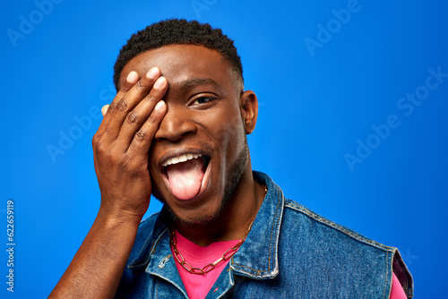 Φωτογραφία Excited young african american man in denim vest and bright t-shirt sticking out