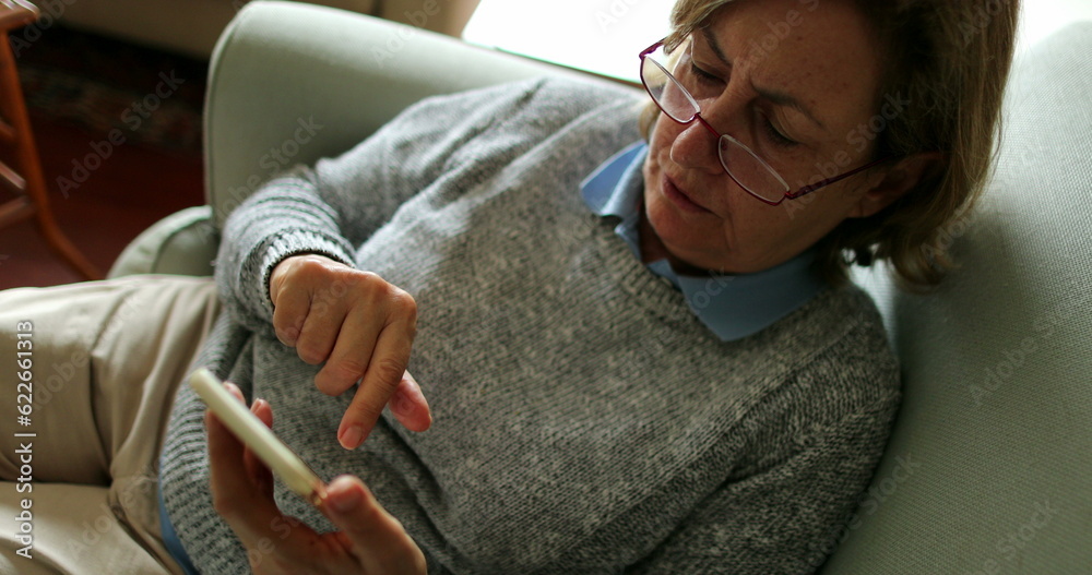 Older woman using phone sitting on couch at home senior person holding smartphone