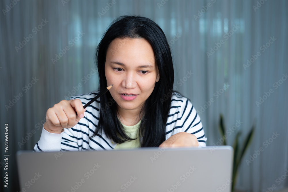 Asian enthusiastic woman in casual clothing working from home on laptop Asian enthusiastic woman in casual clothing working from home on laptop