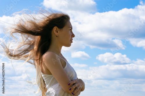 Young long blond haired woman standing upon blue sky background and hugging herself.Concept of sorrowfull, sadness and hope or divorce metaphor. Melancholic or depressed woman photo