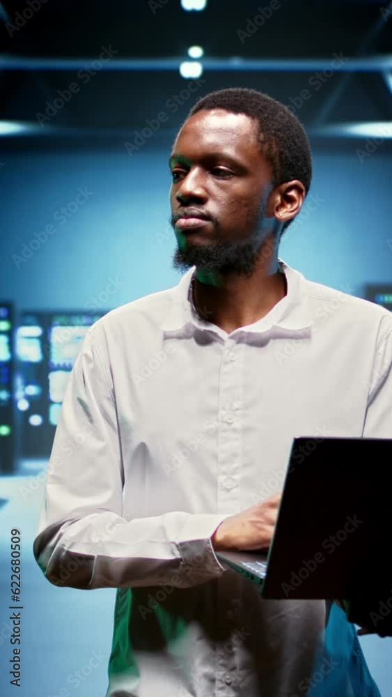 Vertical video African american IT specialist walking between operational mainframes in high performance computing server room, ensuring ideal operations conditions. Expert monitoring equipment energy Vertical video African american IT specialist walking between operational mainframes in high performance computing server room, ensuring ideal operations conditions. Expert monitoring equipment energy