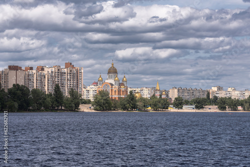 Church on the river bank. Cloudy sky. Urban landscape. Cathedral with domes. Ukrainian culture. Natural beauty of Ukraine.
