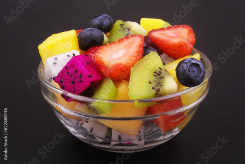 Colorful fruit salad in glass bowl on black background close up. 