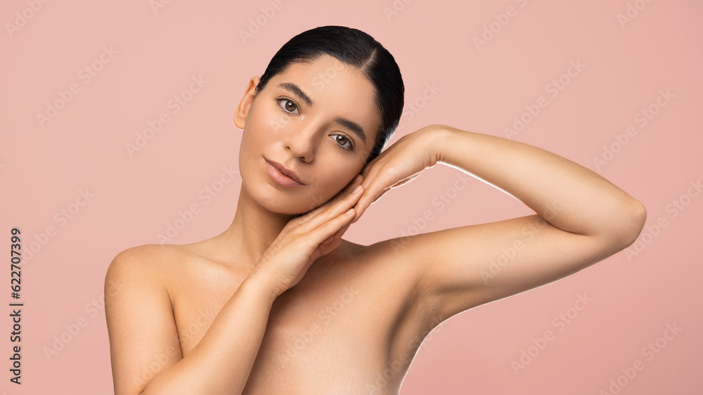 Obraz premium Beauty portrait of multiethnic attractive woman with serene expression holding palms to her face on pink background