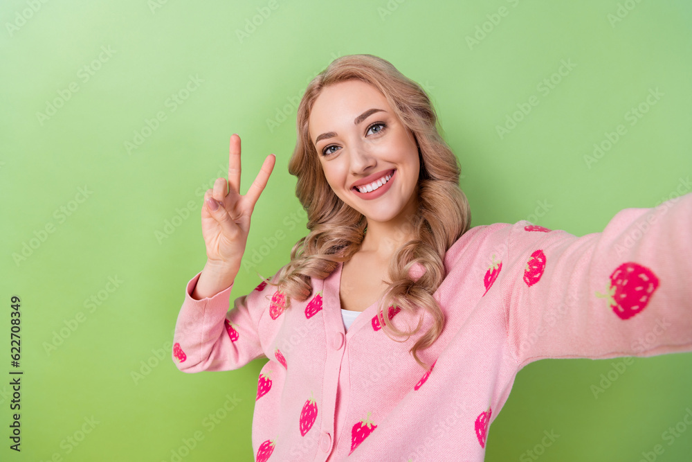 Portrait selfie photo of young friendly girl showing v-sign hello symbol peace blogging video record isolated on green color background Portrait selfie photo of young friendly girl showing v-sign hello symbol peace blogging video record isolated on green color background