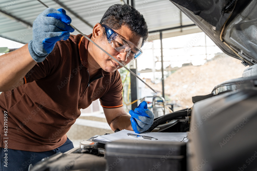 An Asian male car mechanic checking car oil and working on repairing the car at car repair garage