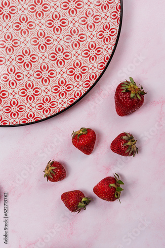 strawberries and red plate on pink marble background
