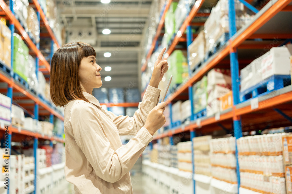Warehouse worker hands holding tablet check stock on tall shelves in warehouse storage. Asian woman auditor or staff work looking up stock taking inventory in cargo store. Owner start up business. Warehouse worker hands holding tablet check stock on tall shelves in warehouse storage. Asian woman auditor or staff work looking up stock taking inventory in cargo store. Owner start up business.