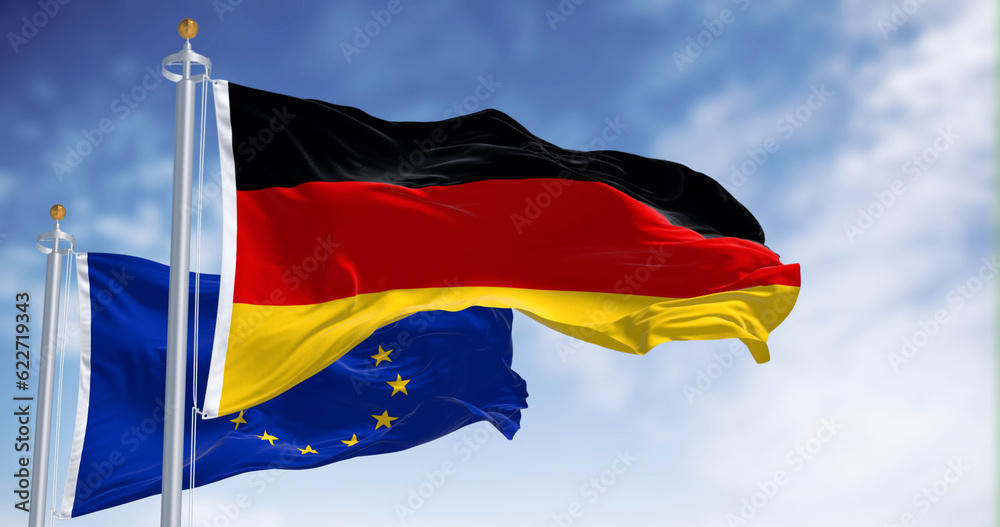The flags of Germany and the European Union waving in the wind on a clear day The flags of Germany and the European Union waving in the wind on a clear day