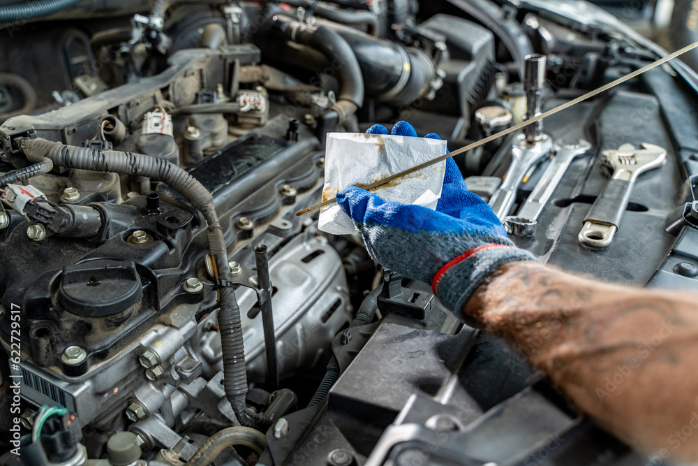 Close up hands of a male car mechanic checking car oil with engine in the background