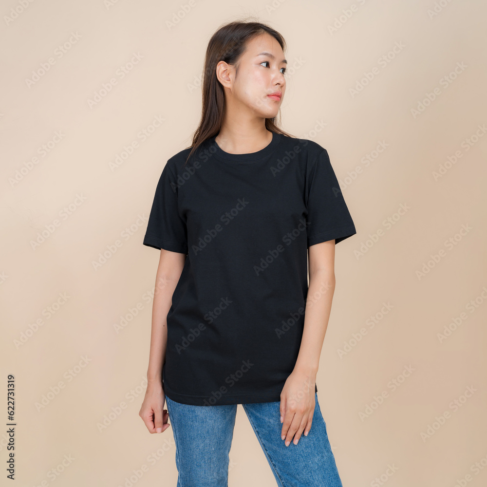 Female fashion model in black t-shirt and jeans standing in studio on beige background Female fashion model in black t-shirt and jeans standing in studio on beige background