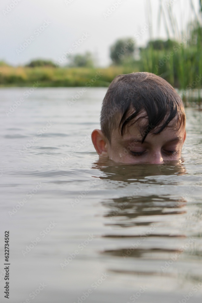 the boy is swimming in the open air in the river in the water while resting on vacation in the village