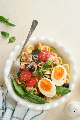 Italian pasta salad. Orecchiette pasta with tuna, tomato cherry, olive, basil and parmesan cheese in plate on grey stone or concrete background. Traditional Italian cuisine. Flat lay. Copy space.