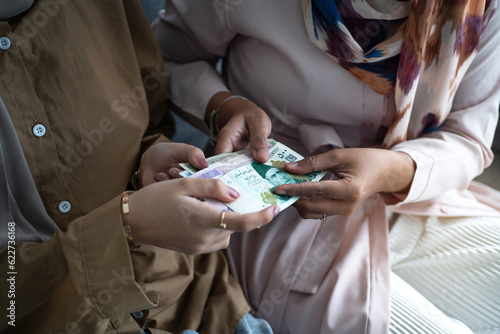 Muslim young girl receive full cash money banknotes during Eid Fitri or Hari Raya celebration, Islamic Zakat or Sadaka concept photo