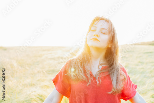 A happy woman with closed eyes relaxing in wheat field on sunset. Breathe of freedom. Positive emotions feeling life, peace of mind. Mental health practice. Nature relaxation. Selective focus