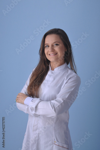 médica jovem sorridente usando uniforme branco em fundo azul, expressão feliz apontando para anúncio ou promoção  © Alexandre
