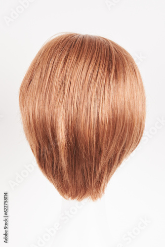 Natural looking ginger wig on white mannequin head. Short hair on the plastic wig holder isolated on white background, back view.