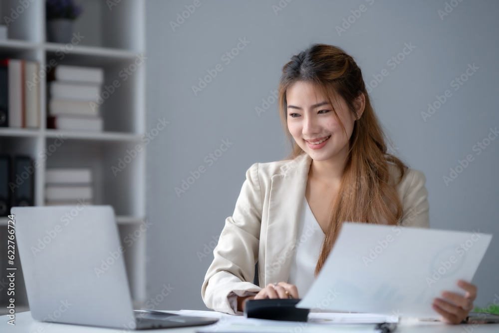 Beautiful young business woman manager or company worker holding accounting document, checking financial data or marketing report working in office with laptop. Accountant consults on some docum. Beautiful young business woman manager or company worker holding accounting document, checking financial data or marketing report working in office with laptop. Accountant consults on some docum.