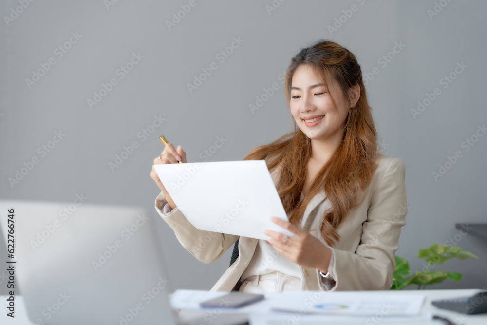 Beautiful young business woman manager or company worker holding accounting document, checking financial data or marketing report working in office with laptop. Accountant consults on some docum. Beautiful young business woman manager or company worker holding accounting document, checking financial data or marketing report working in office with laptop. Accountant consults on some docum.