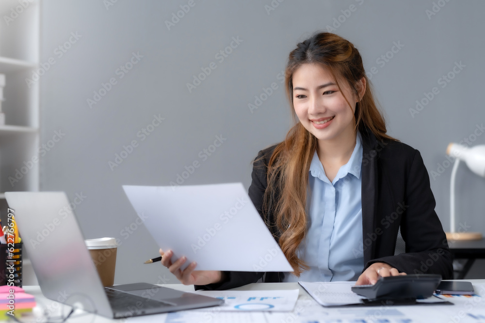 Beautiful young business woman manager or company worker holding accounting document, checking financial data or marketing report working in office with laptop. Accountant consults on some docum. Beautiful young business woman manager or company worker holding accounting document, checking financial data or marketing report working in office with laptop. Accountant consults on some docum.