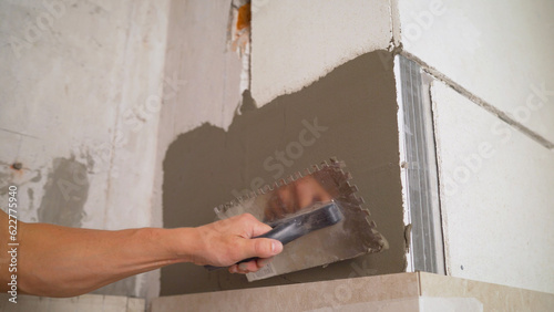 The adhesive solution is applied to the wall. Putty on the wall, for gluing ceramic tiles. Laying gypsum tiles on gypsum wall adhesive with a spatula. Applying an adhesive solution.