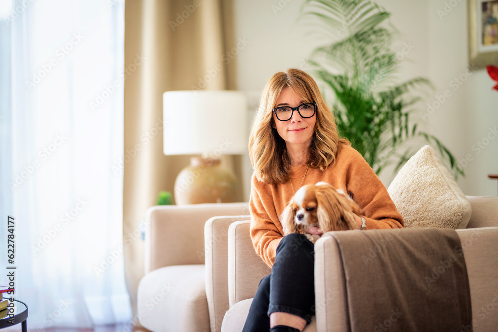 Mid aged woman with blond hair relaxing in an armchair at home with her cute puppy Mid aged woman with blond hair relaxing in an armchair at home with her cute puppy