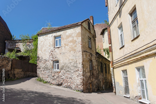 Fototapeta Naklejka Na Ścianę i Meble -  Street in the old town with a two-story stone house with crumbling plaster with trees growing on the roof