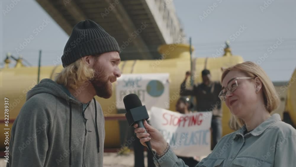 DescriptionYoung male environmental activist giving interview to TV journalist during protest against pollution, people with posters in background