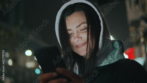 Girl's face illuminated by a smartphone screen in a hood in the rain at night